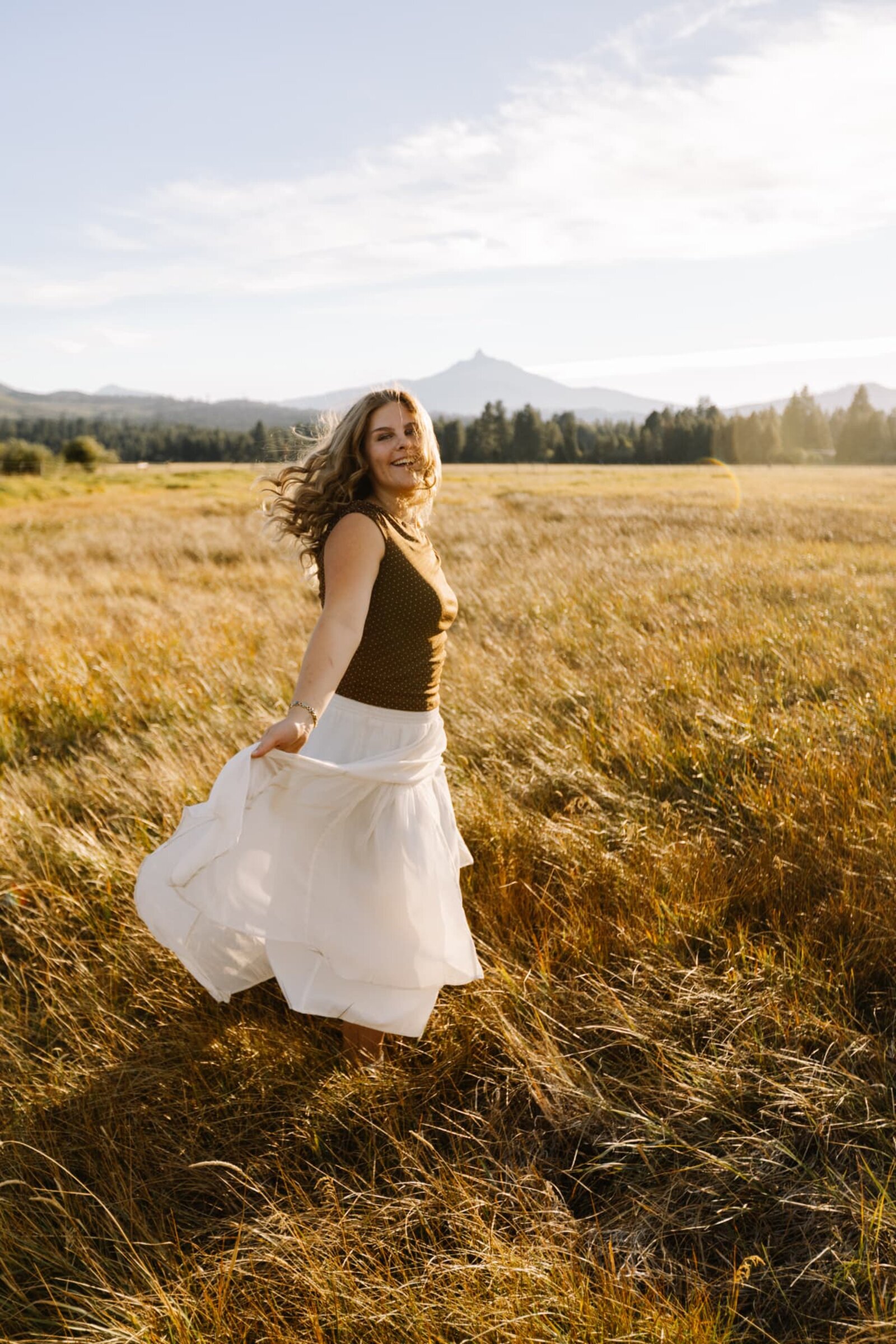 Senior girl twirling in a golden meadow with a Cascade peak on the horizon