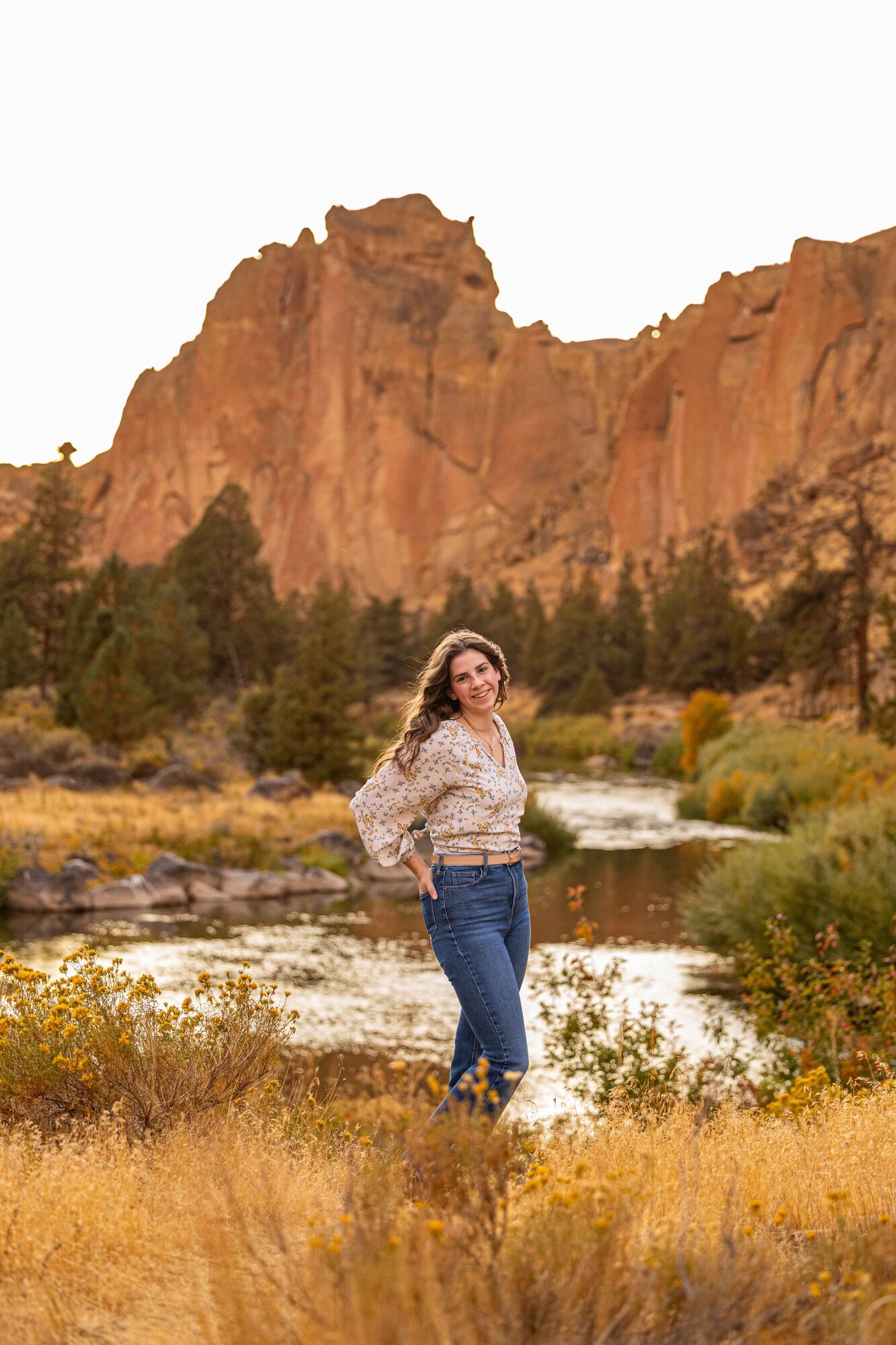 Senior girl in a floral top by the Crooked River with Smith Rock spires behind her