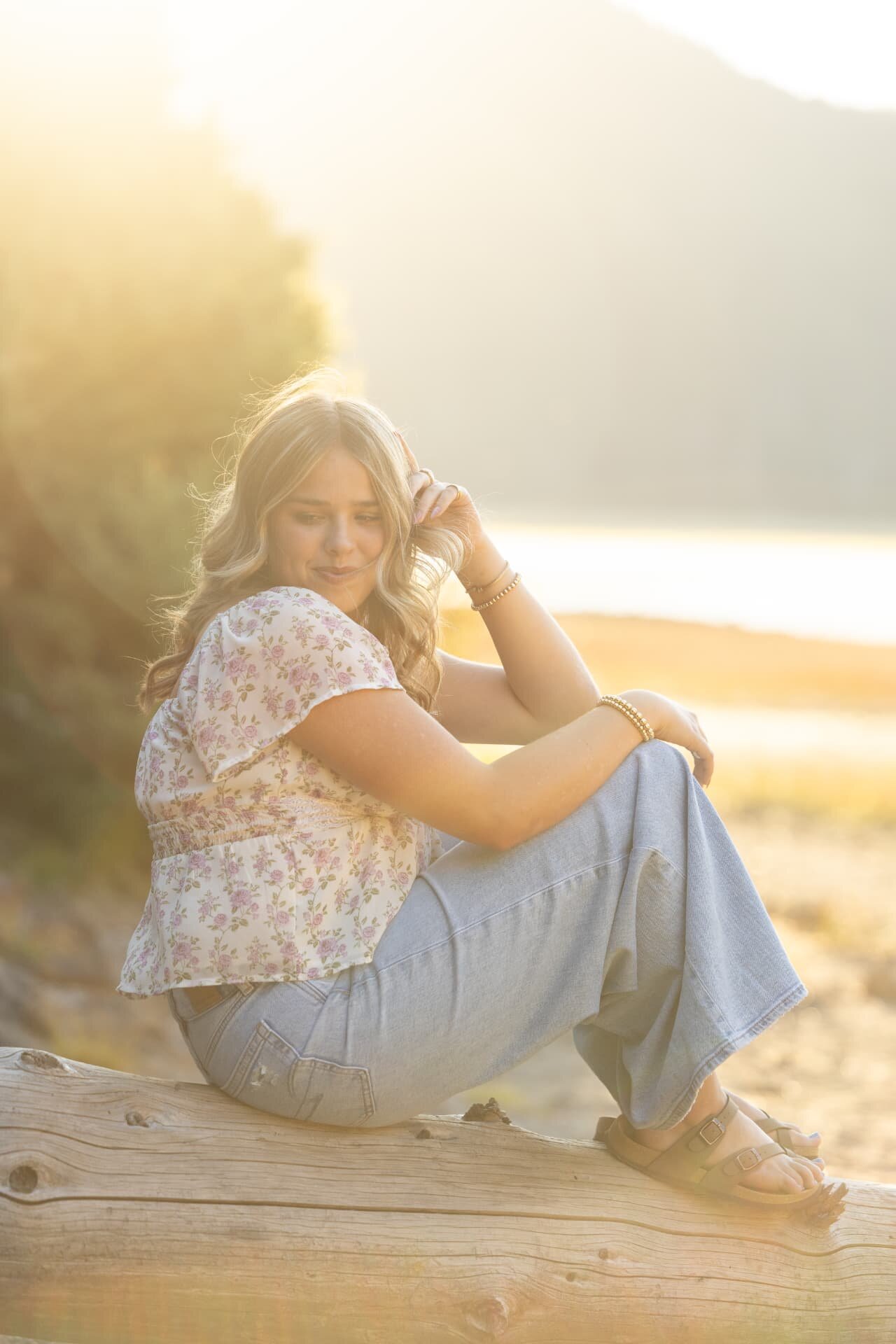 Senior girl sitting on a fallen log in hazy golden sunset light