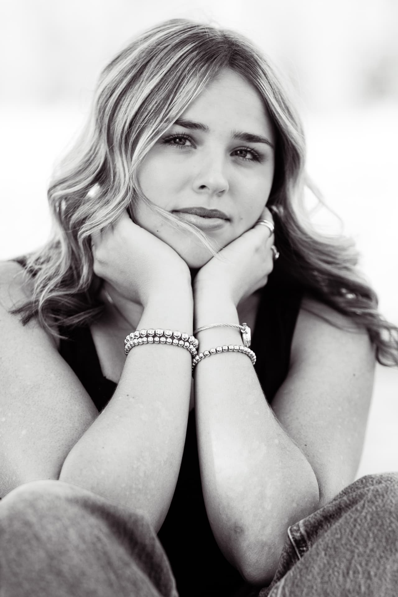 Black and white senior portrait of a girl with her chin resting on her hands