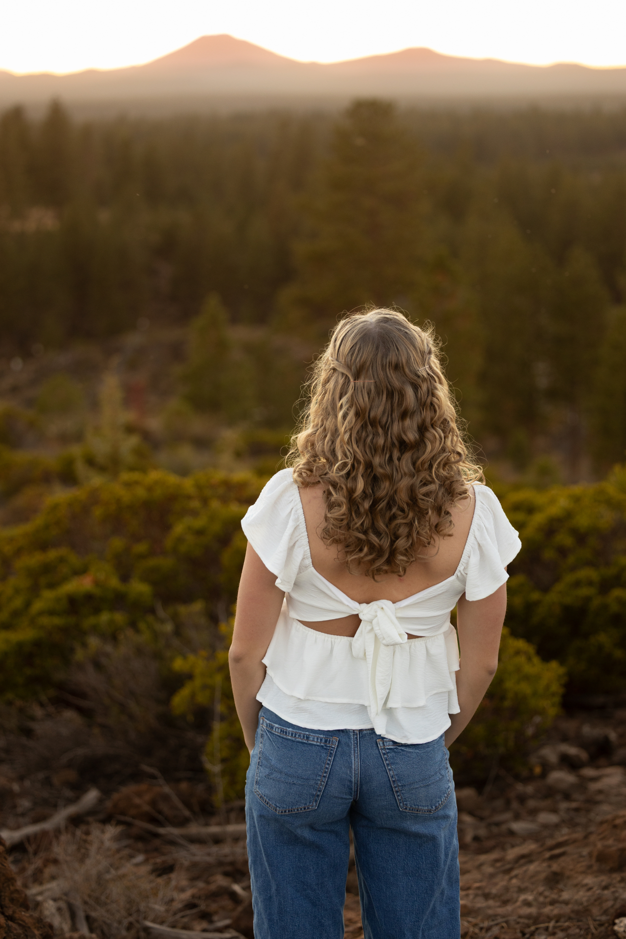 Senior girl looking over the forest toward the Cascade mountains at sunset