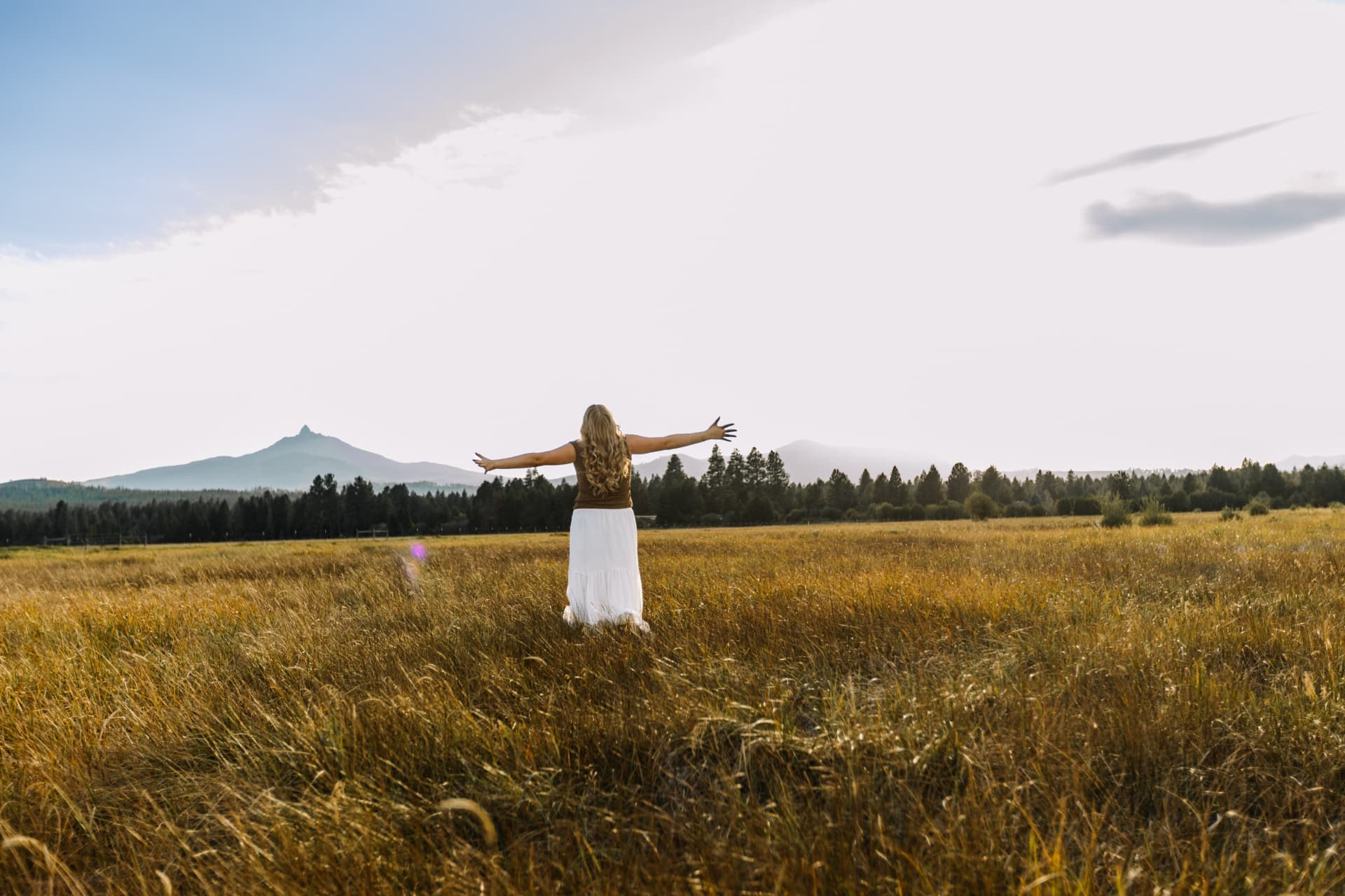 Senior girl with arms wide open in a golden field with Mount Washington on the horizon