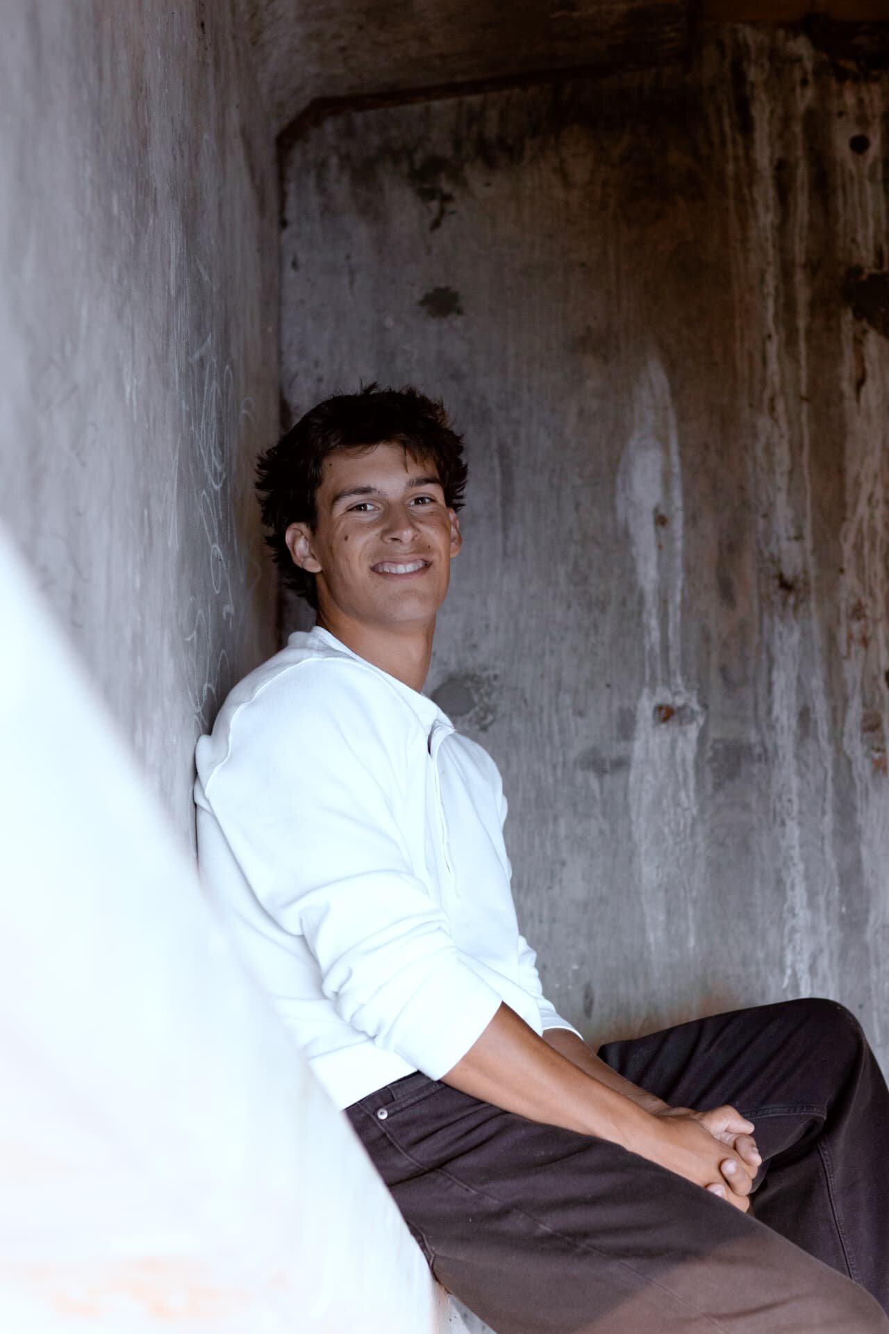 Senior guy smiling while leaning against a weathered concrete wall