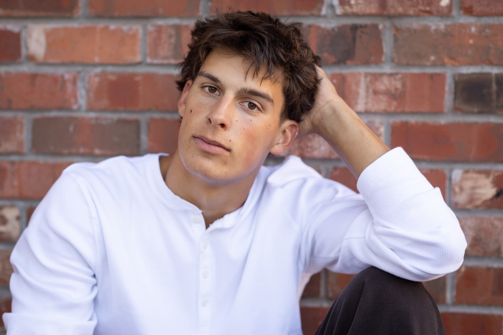 Close up senior portrait of a guy against a brick wall