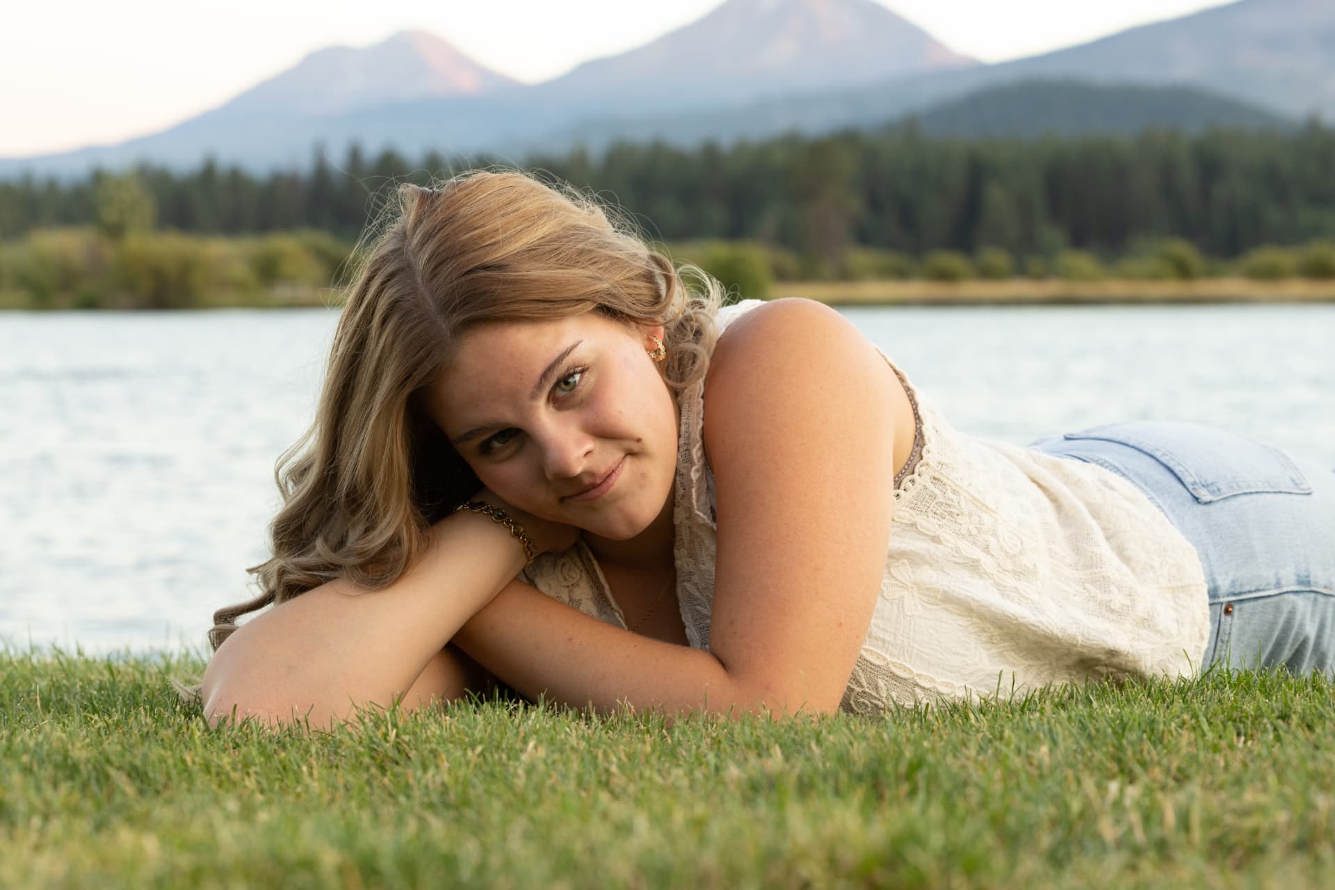Senior girl lying in the grass beside a lake with the Three Sisters behind her