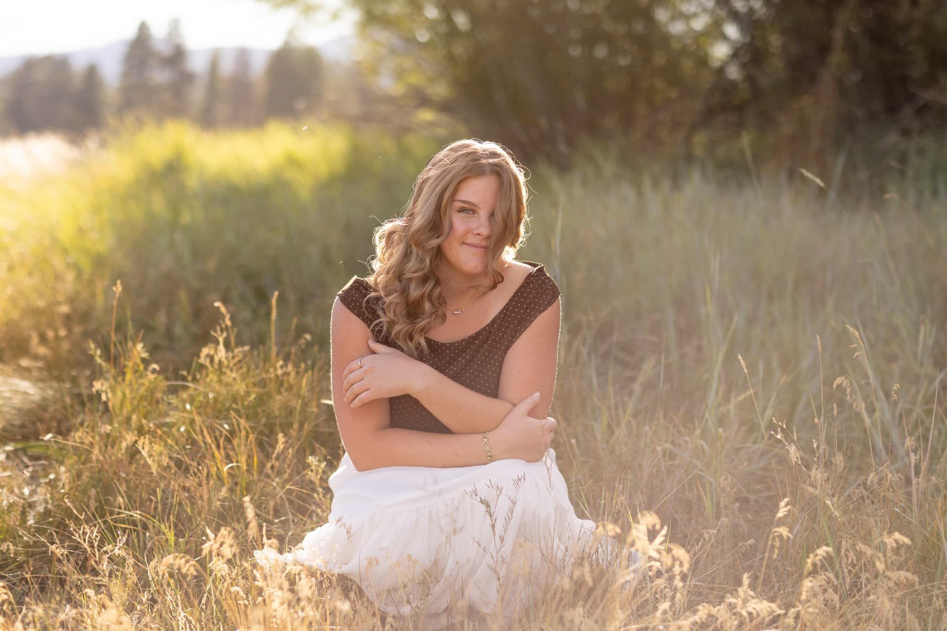 Senior girl kneeling in tall backlit grass at golden hour