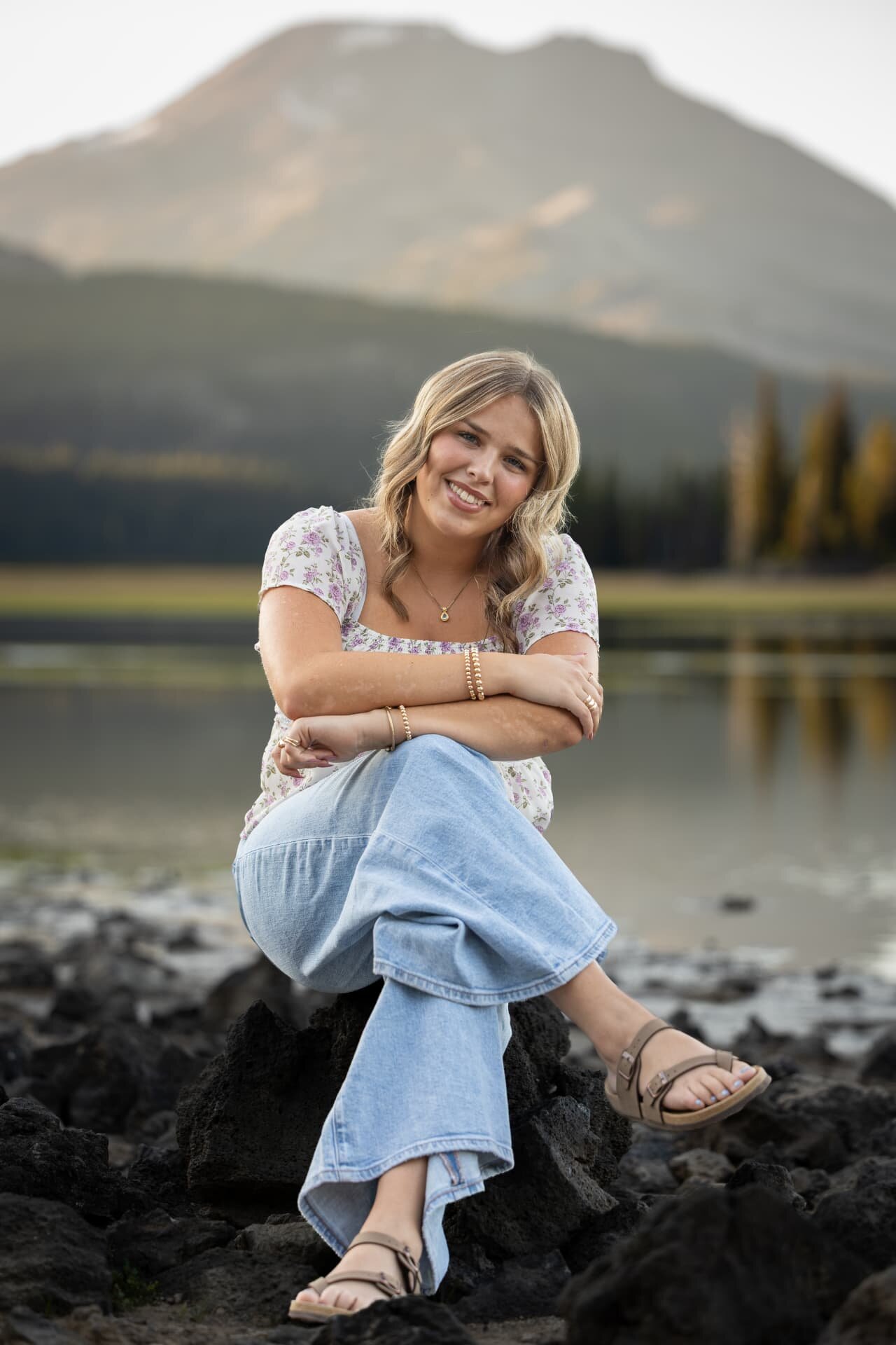 Senior girl seated on lava rock at Sparks Lake with South Sister reflected behind
