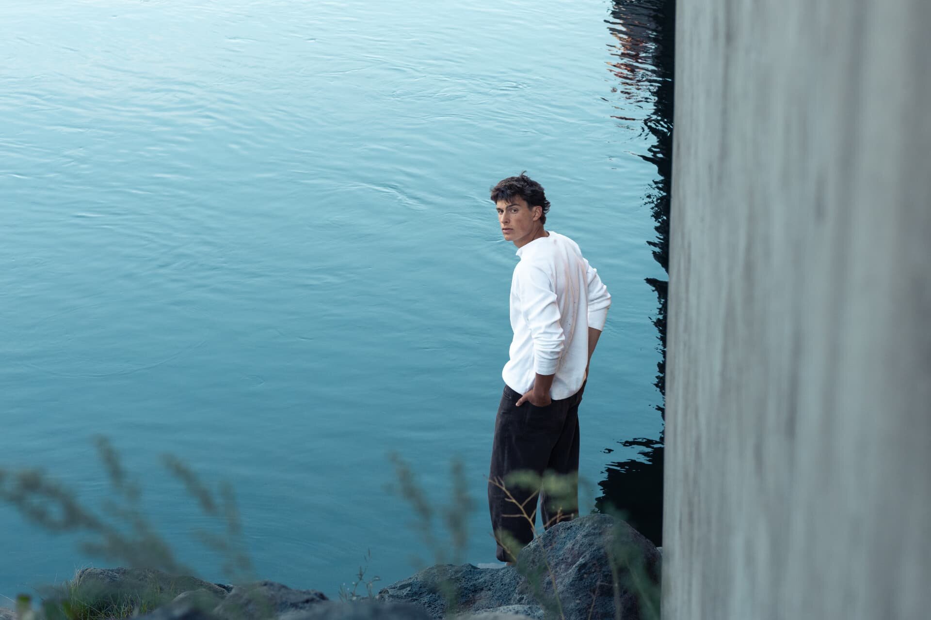 Senior guy looking back over his shoulder beside still teal river water