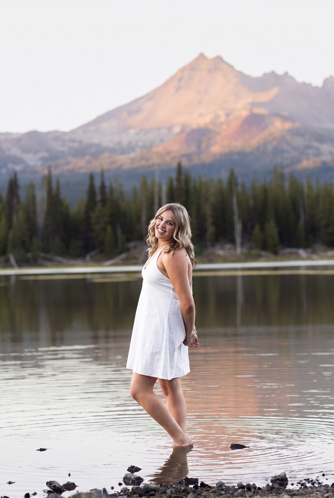 Senior standing in the shallows of Sparks Lake below Broken Top