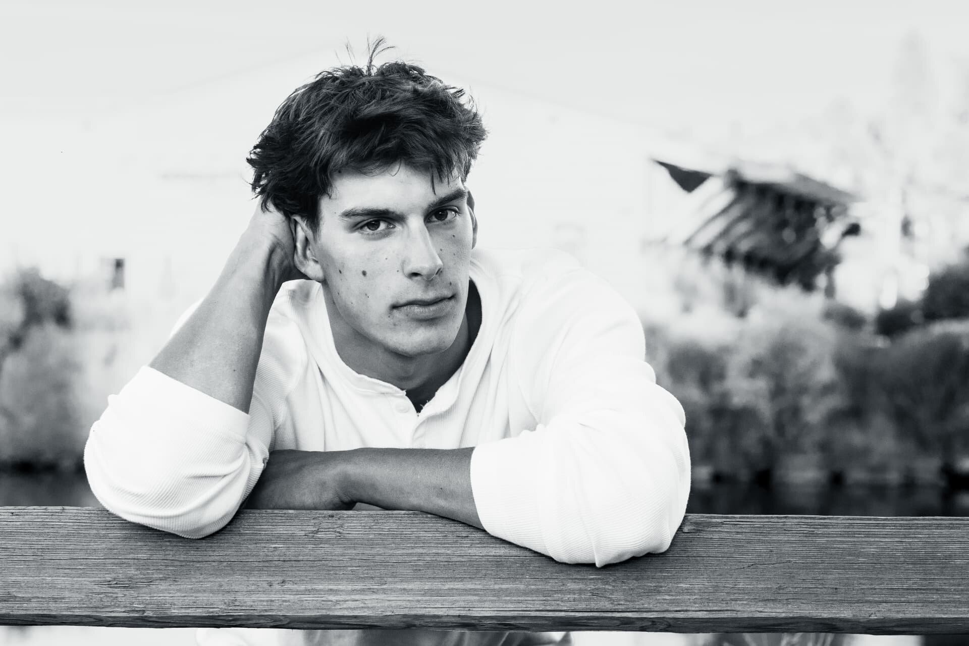 Black and white senior portrait of a guy leaning on a wooden rail