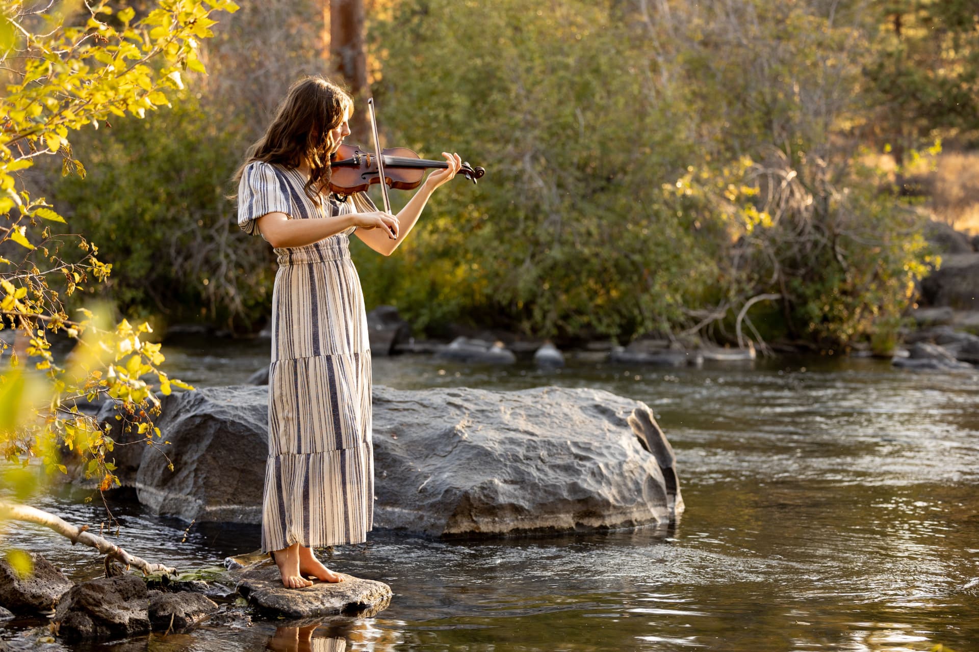 Senior girl playing violin while standing on a river rock in the Crooked River