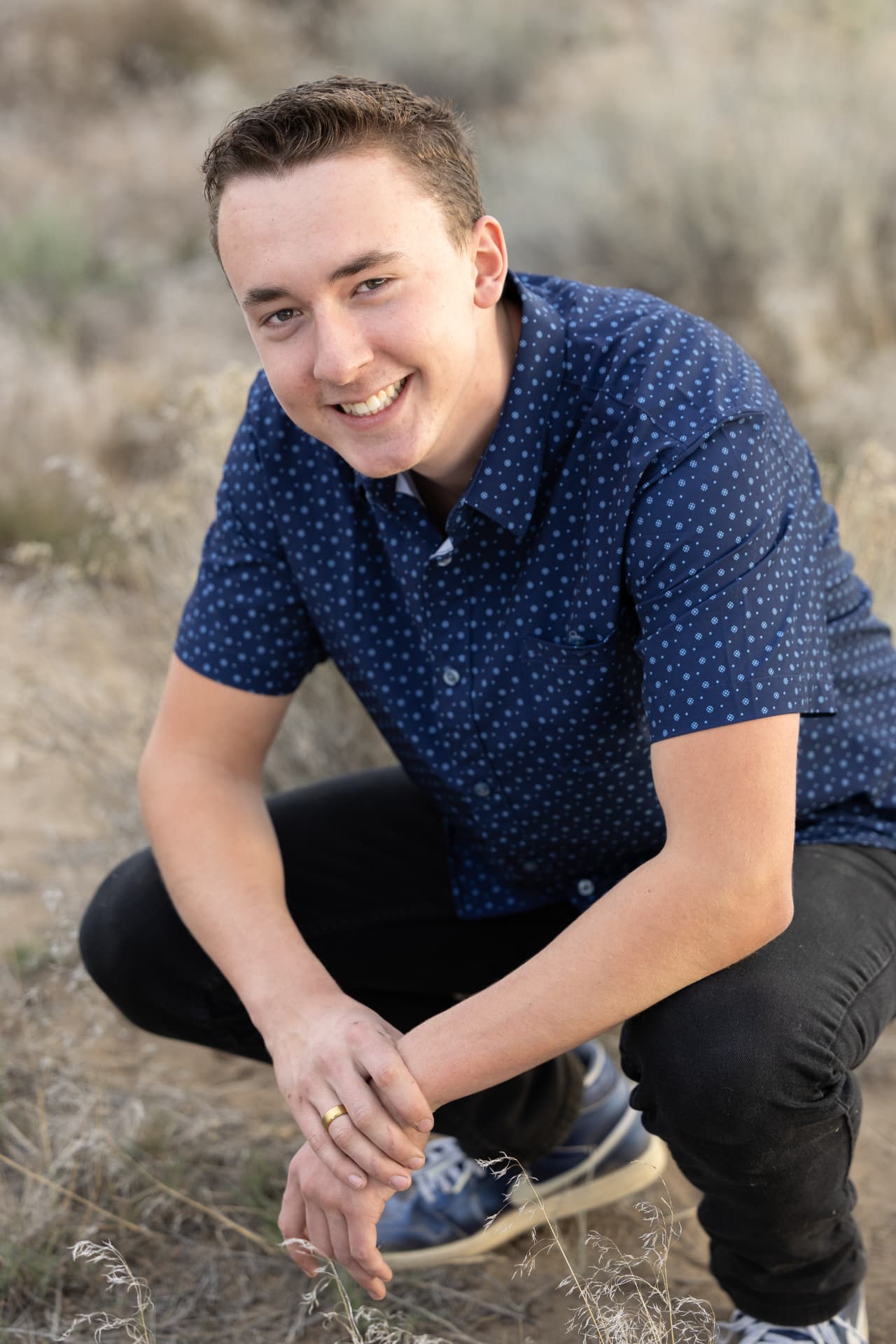 Senior guy crouching in dry high desert grass at golden hour