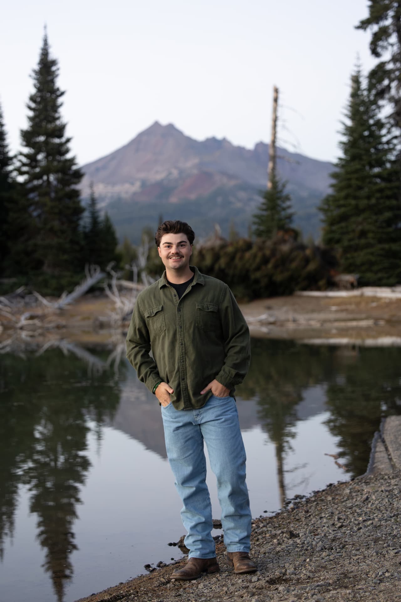 Senior guy standing beside a mountain lake with a Cascade peak behind him