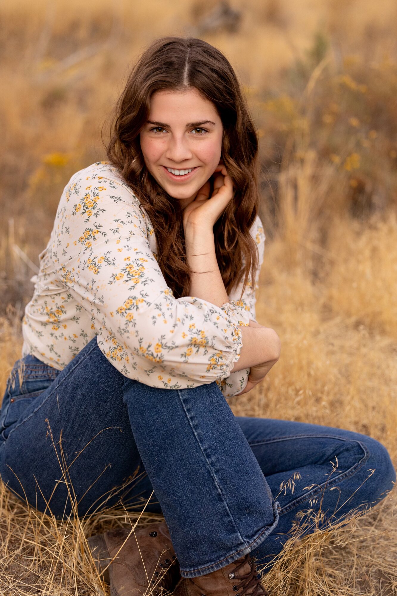 Senior girl in a floral top smiling while sitting in golden high desert grass