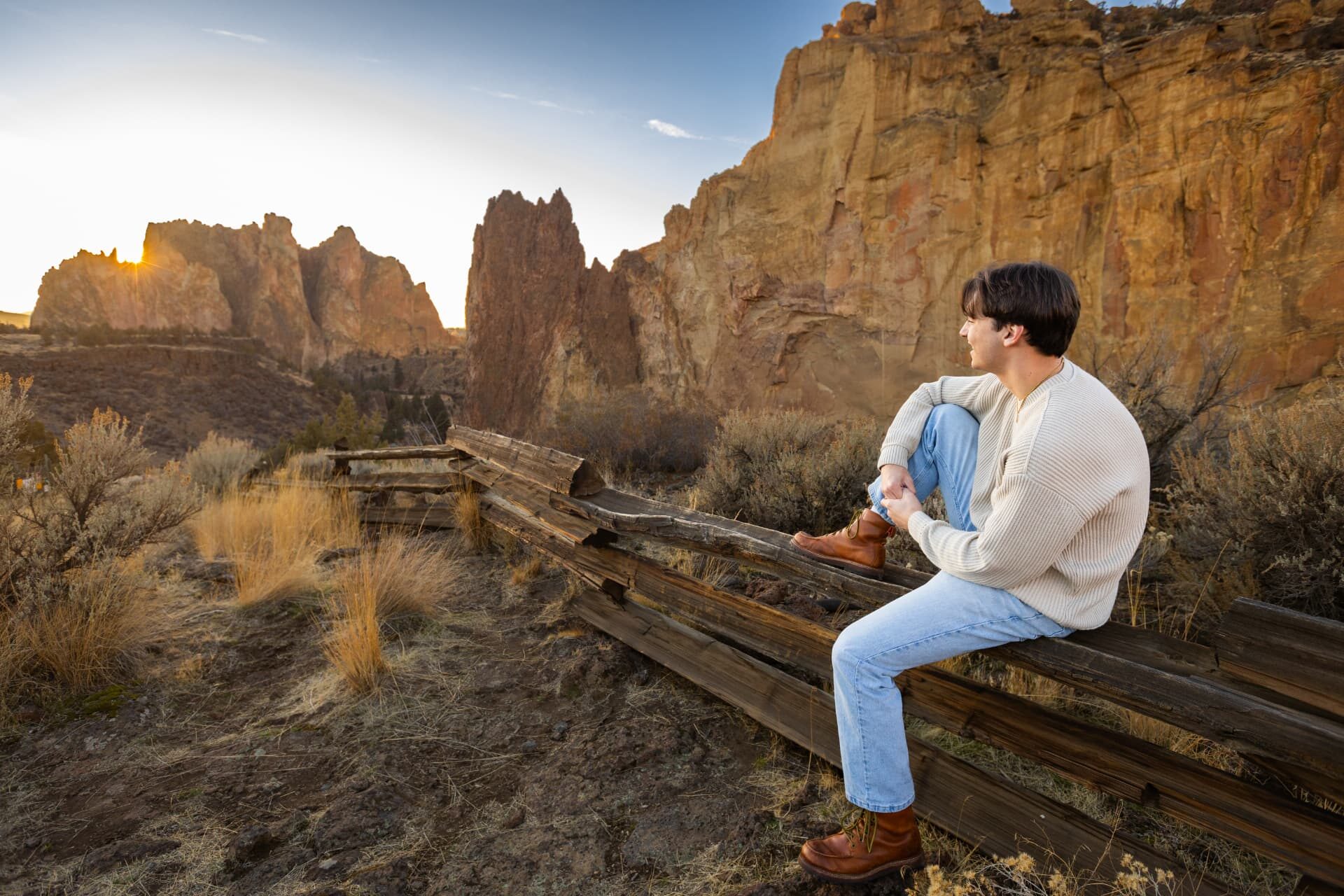 Senior sitting on a weathered rail fence as the sun sets behind Smith Rock