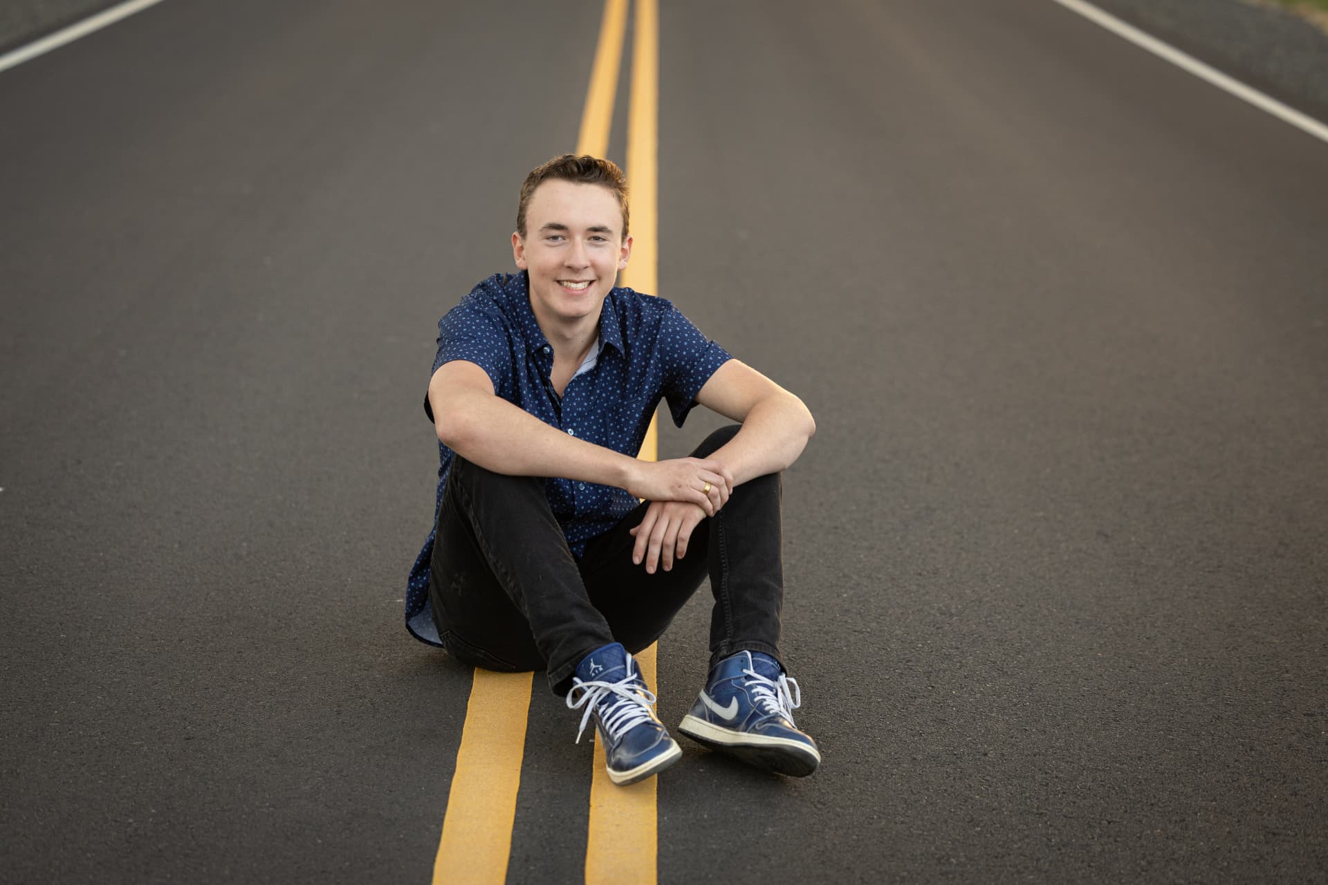 Senior guy sitting on a double yellow line on an empty back road