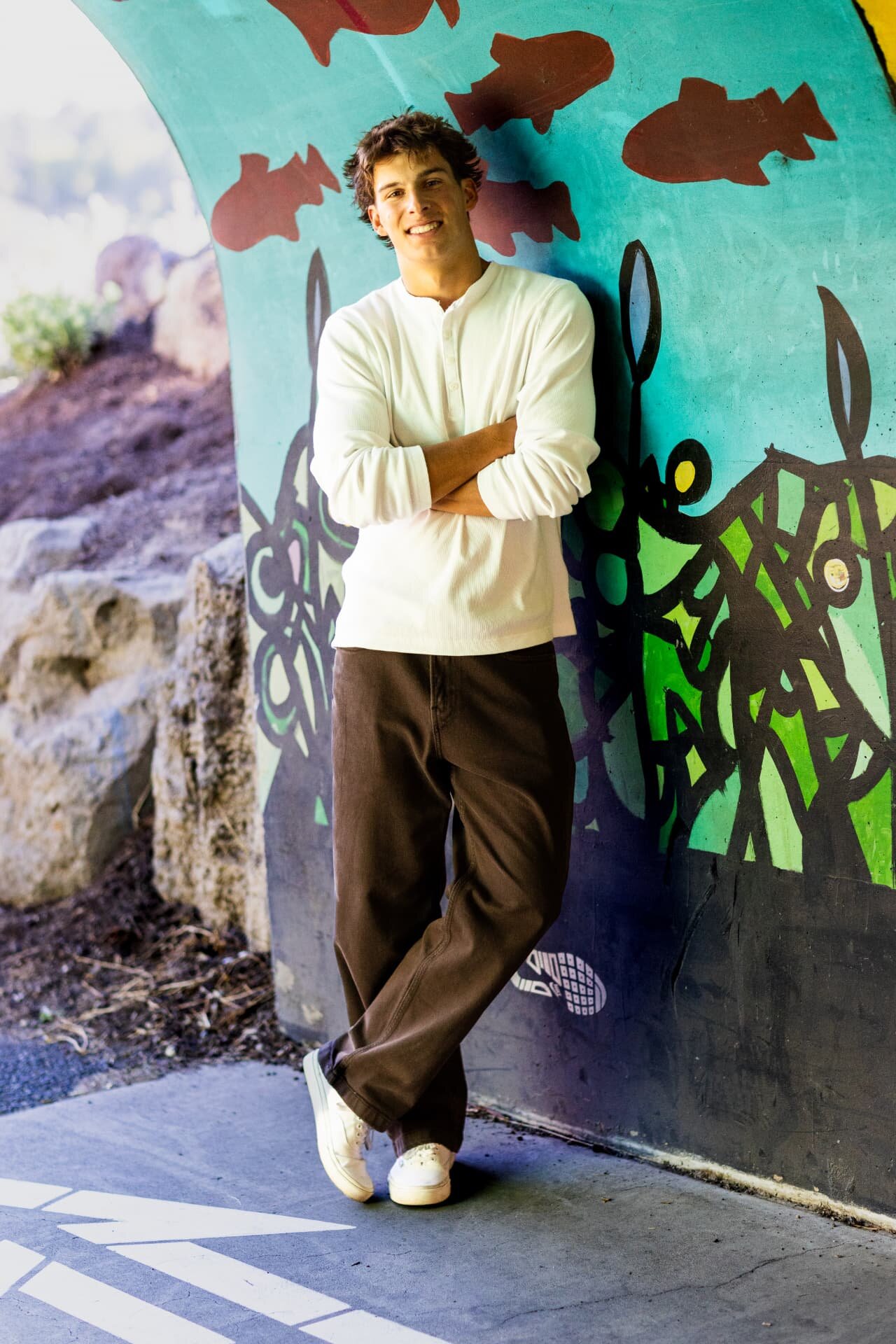 Senior guy leaning against a colorful painted mural underpass in Bend