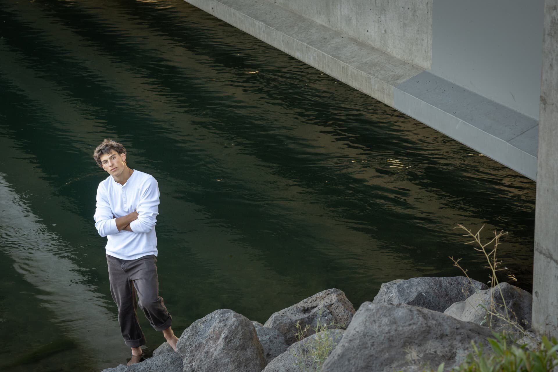 Senior guy standing at the river's edge beneath a bridge in Bend