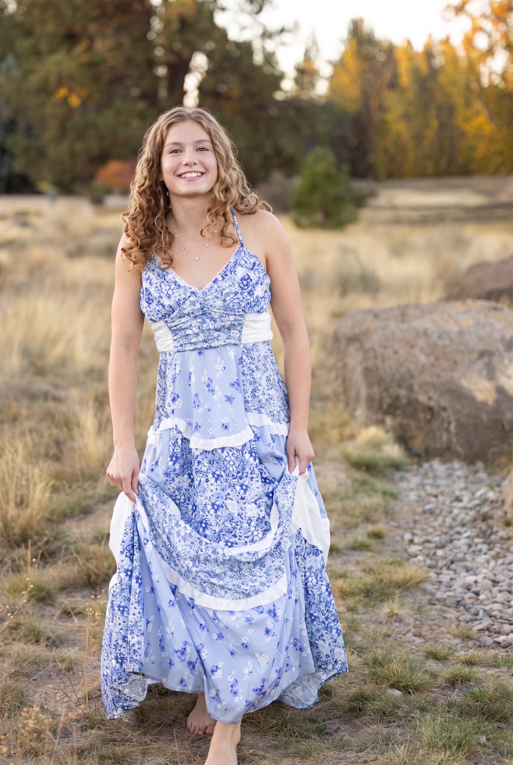 Senior girl standing in a blue floral dress beside autumn aspens