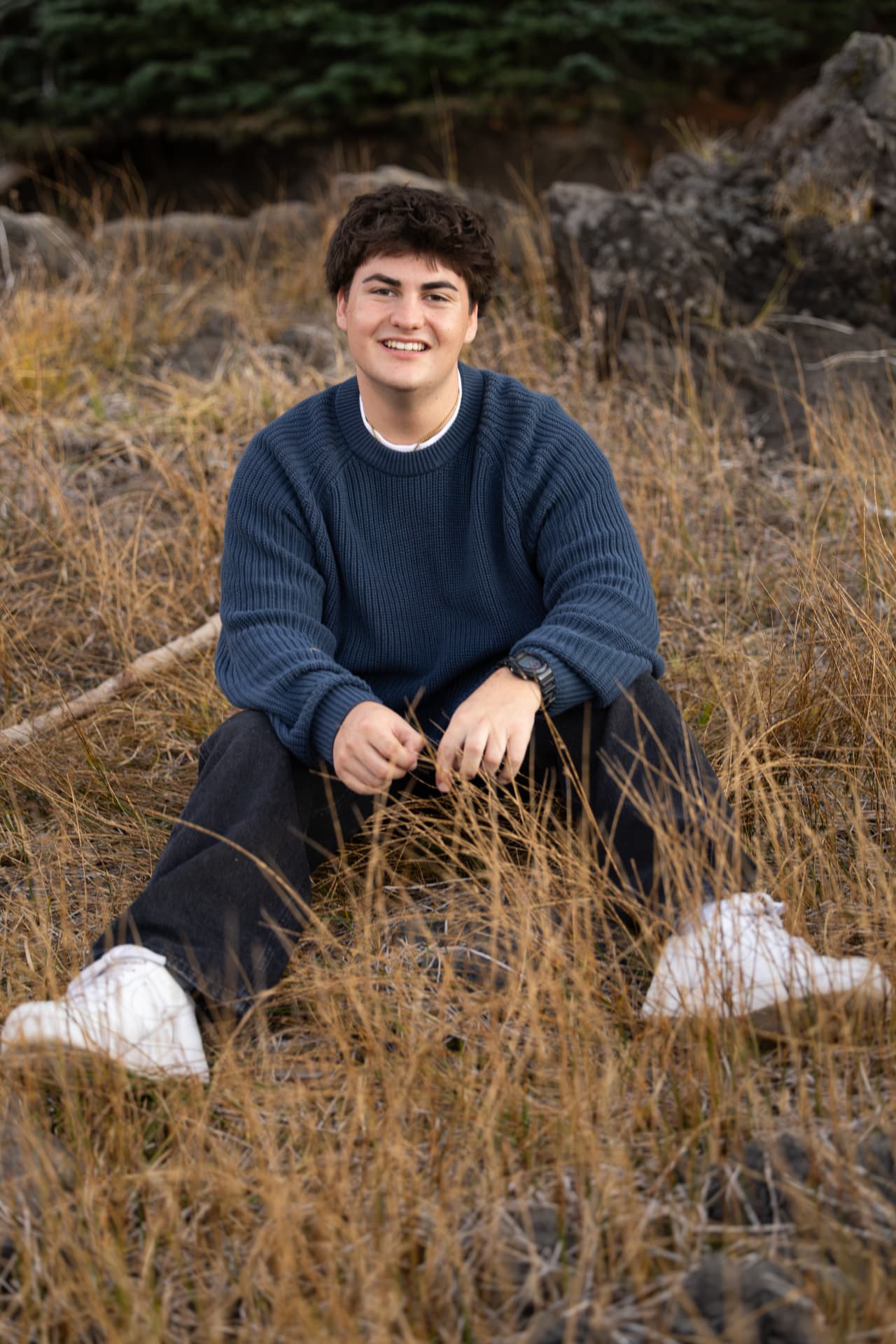 Senior guy in a navy sweater sitting in golden grass at Sparks Lake
